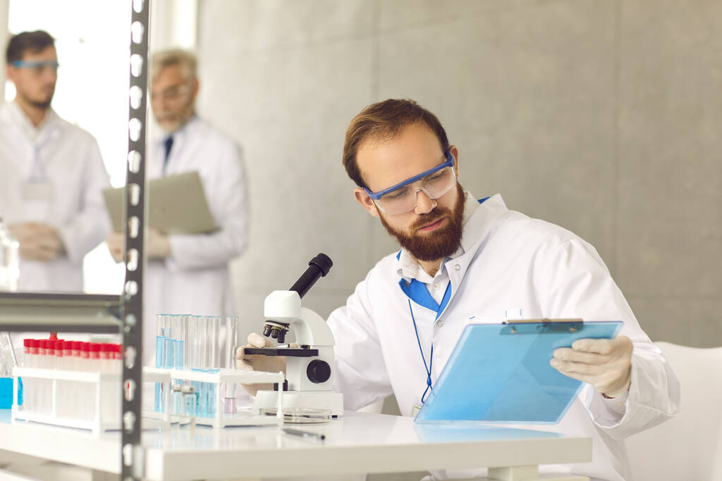 Porträt eines Wissenschaftlers, der auf Klemmbrett mit Testergebnissen im Labor blickt - Foto, Bild