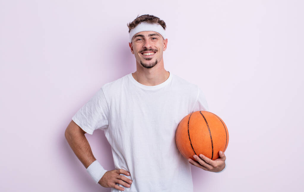 young handsome man smiling happily with a hand on hip and confident. basketball concept - Photo, Image