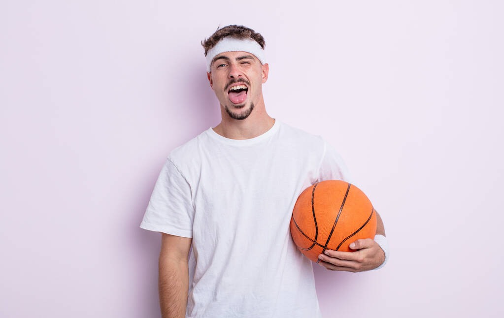 Молодой красивый мужчина с веселым и бунтарским отношением, шутит и высовывает язык. баскетбол - Фото, изображение