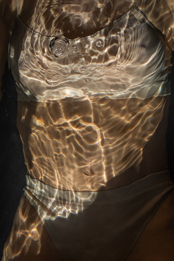 Сексуальная женщина в бежевом белье лежит в воде на темном фоне. - Фото, изображение