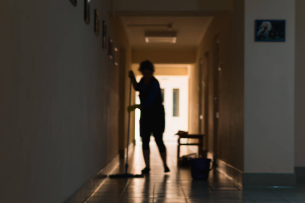 Θολή εικόνα γυναίκας που καθαρίζει το χώρο κατά τον καθαρισμό του διαδρόμου και του γραφείου - Φωτογραφία, εικόνα