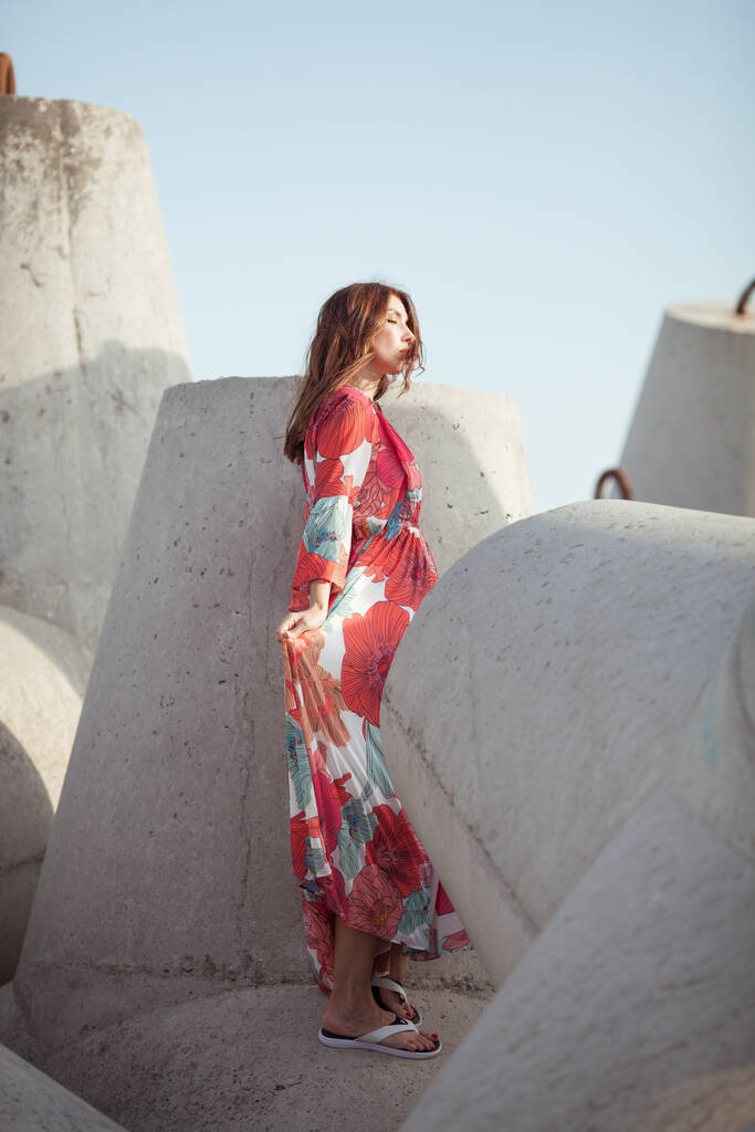 Hermosa mujer en un vestido rojo largo cerca del rompeolas, un paseo por el mar - Foto, imagen