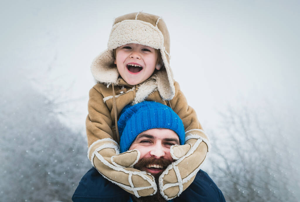 Daddy and boy smiling and hugging. Father giving son ride on back in winter park. Merry Christmas and Happy New Year. Portrait of happy father and son. - Photo, Image