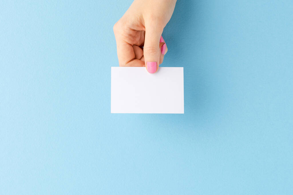 Γυναικείο χέρι που δείχνει λευκή επαγγελματική κάρτα σε μπλε φόντο. Κοπάδι - Φωτογραφία, εικόνα