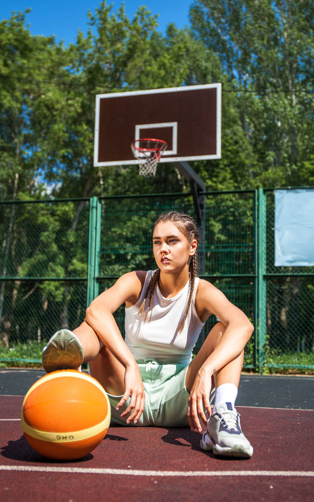 Νεαρή όμορφη μελαχρινή που ποζάρει στο γήπεδο μπάσκετ - Φωτογραφία, εικόνα