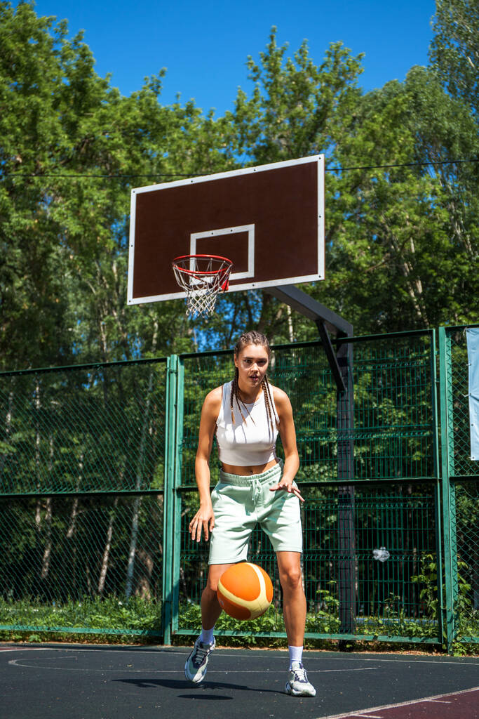 Νεαρή όμορφη μελαχρινή που ποζάρει στο γήπεδο μπάσκετ - Φωτογραφία, εικόνα