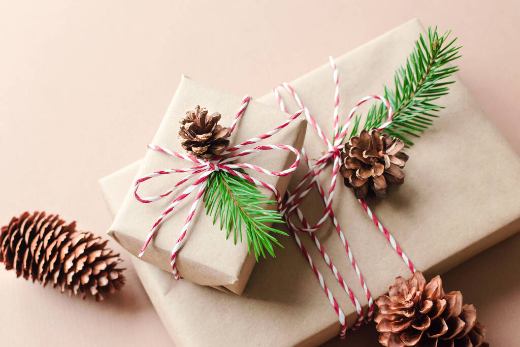 Рождественские подарочные коробки, украшенные елочными ветками и конусами на бежевом фоне - Фото, изображение