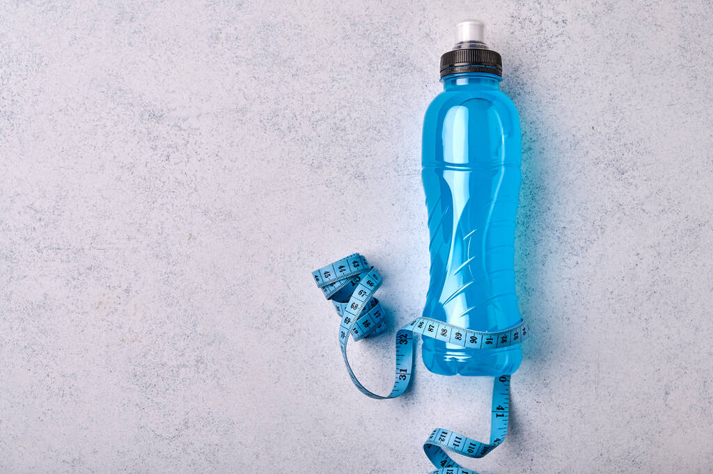 Izotóniai energia kék átlátszó sport ital műanyag palackban és mérőszalag szürke texturált háttér - Fotó, kép