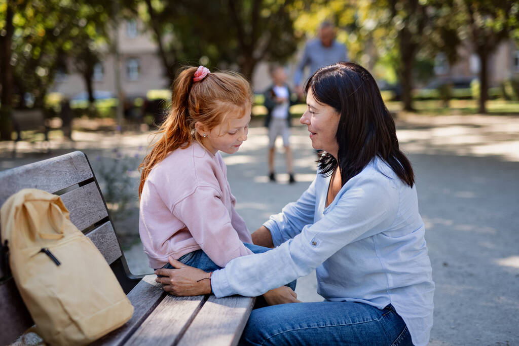 Femme âgée accroupie et parlant à sa petite-fille à l'extérieur sur un banc dans le parc. - Photo, image