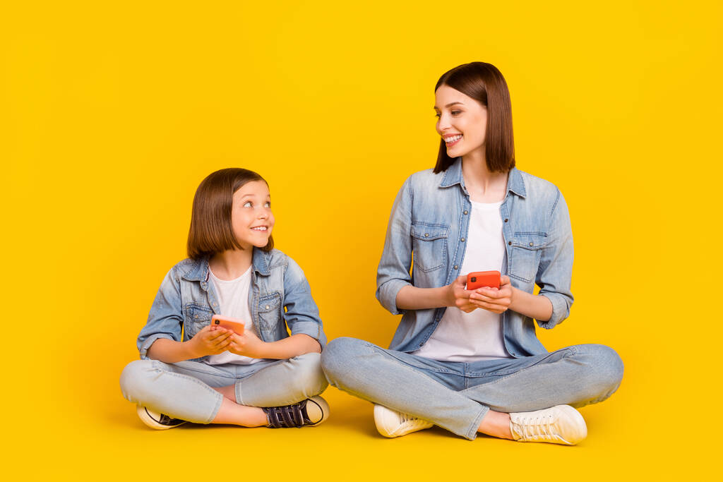 Kuva viehättävä söpö sisarukset pukeutunut denim paitoja istuu lattialla tilalla moderni vempaimia hymyillen eristetty keltainen väri tausta. - Valokuva, kuva