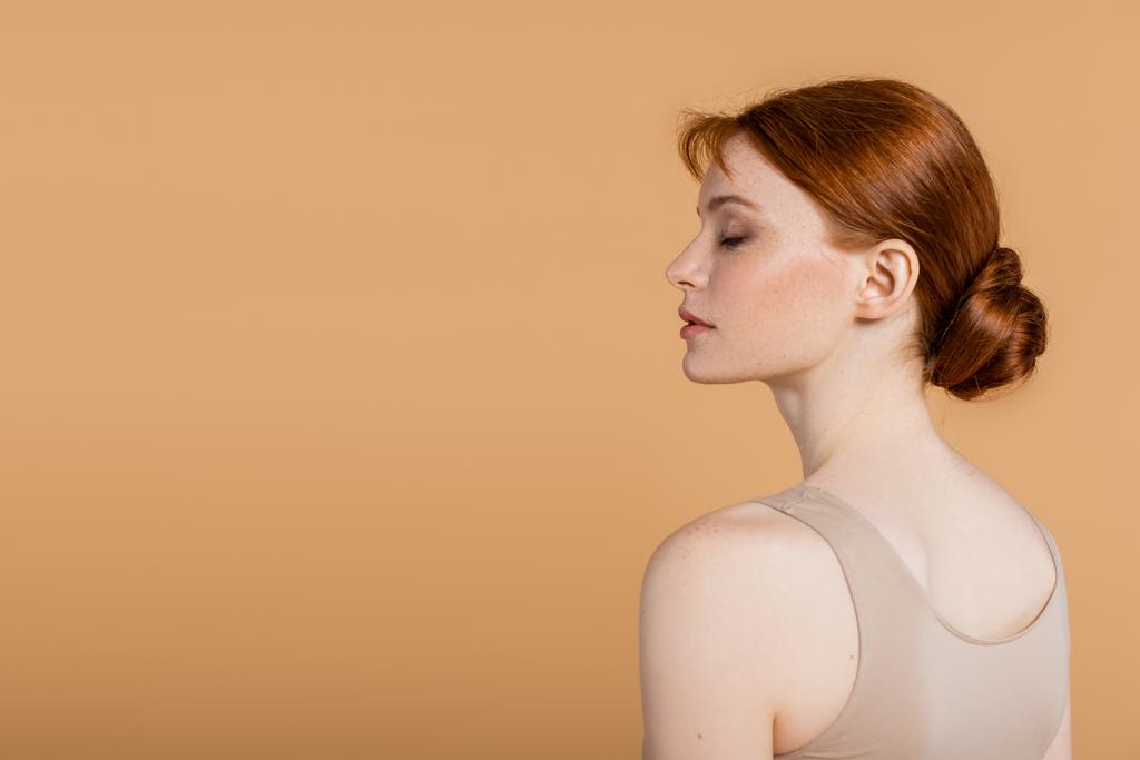 Vue latérale de la jeune rousse femme debout isolé sur beige  - Photo, image