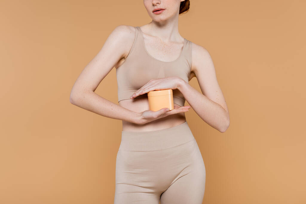 Vista ritagliata di giovane donna in alto tenuta crema cosmetica isolata su beige  - Foto, immagini