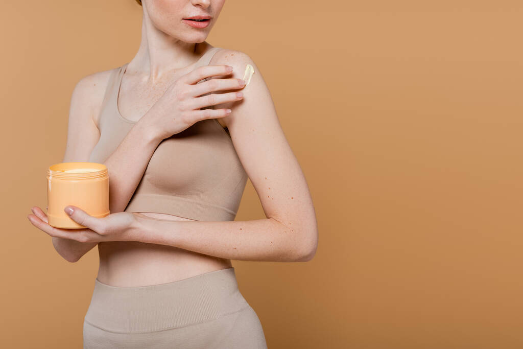 Vista recortada de la mujer pecosa aplicando crema aislada en beige  - Foto, imagen