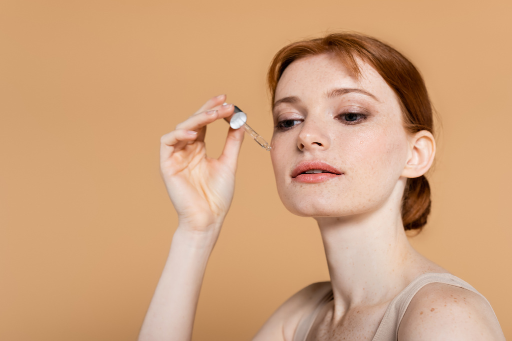 mooie vrouw met schone huid aanbrengen cosmetisch serum geïsoleerd op beige  - Foto, afbeelding