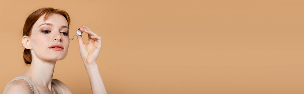 Csinos nő alkalmazó kozmetikai szérum pipetta izolált bézs, banner  - Fotó, kép