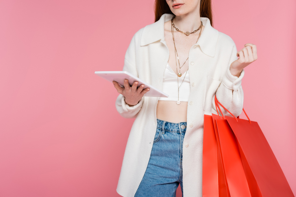 Vágott kilátás elegáns nő gazdaság bevásárlótáskák és digitális tabletta elszigetelt rózsaszín - Fotó, kép