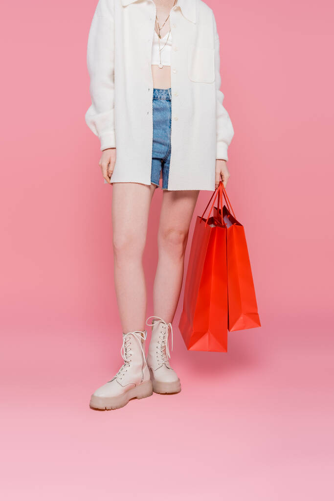 Oříznutý pohled na mladé stylové ženy držící nákupní tašky na růžovém pozadí - Fotografie, Obrázek