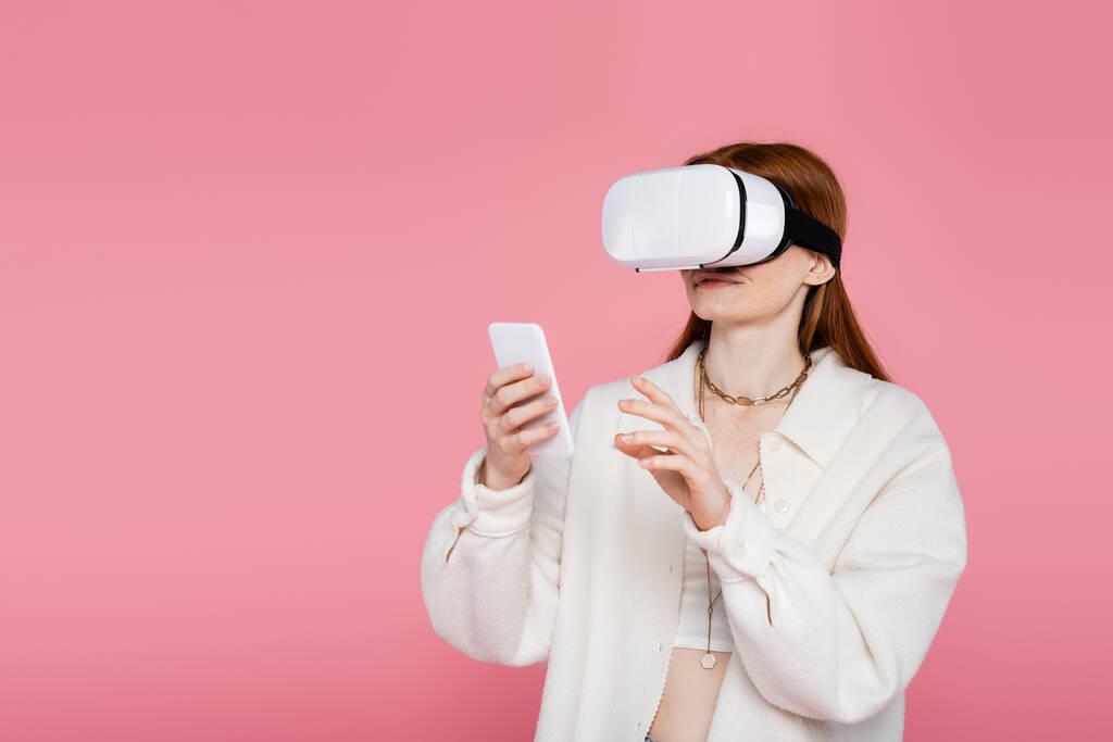 Tyylikäs punapää nainen virtuaalitodellisuus kuulokkeet matkapuhelimella eristetty vaaleanpunainen  - Valokuva, kuva