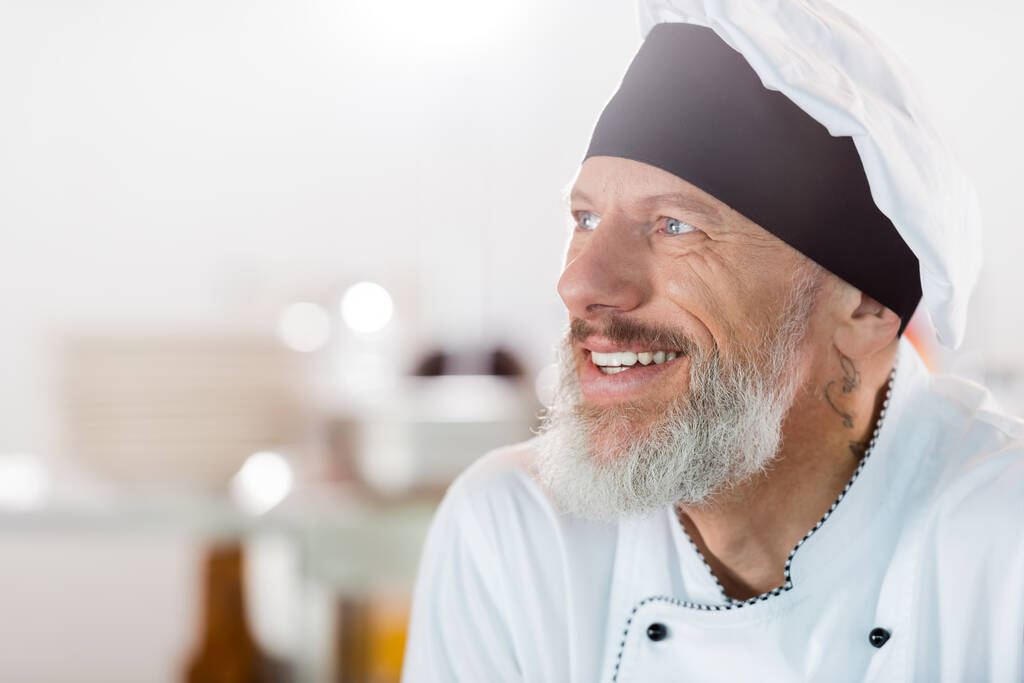 Πορτρέτο του χαμογελαστού σεφ κοιτάζοντας μακριά στην κουζίνα  - Φωτογραφία, εικόνα