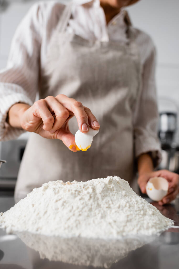 Vista recortada del chef vertiendo huevo sobre harina en la mesa de la cocina  - Foto, imagen