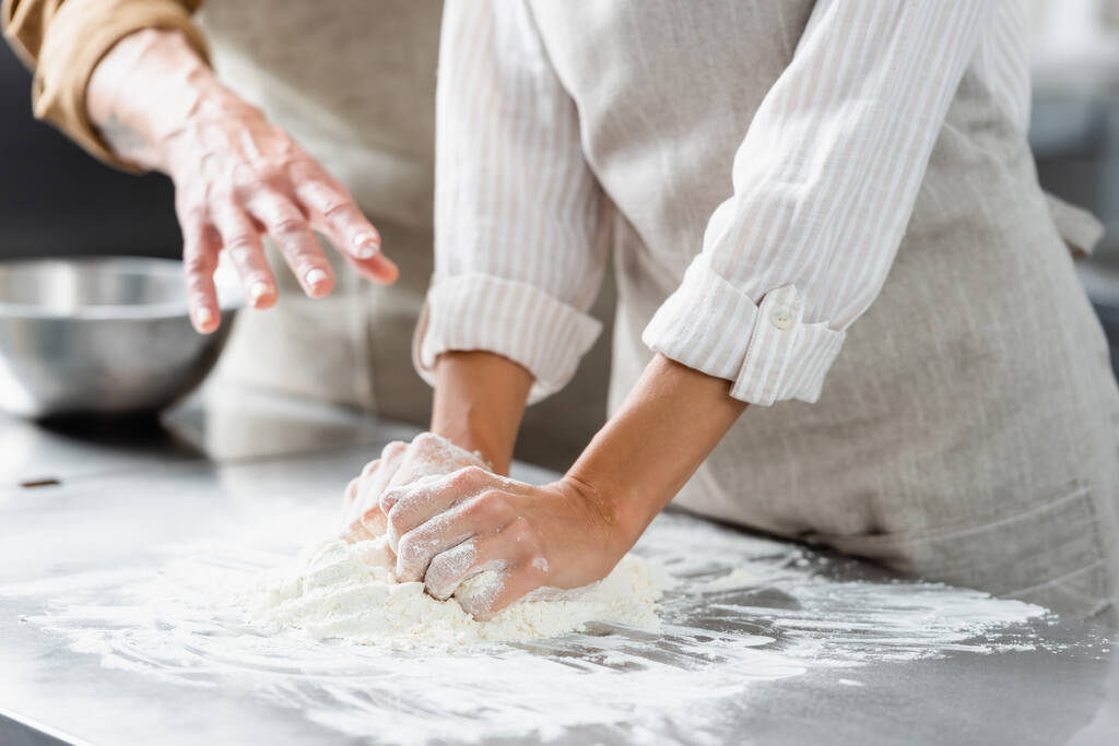 Vue recadrée du chef faisant la pâte près de son collègue pointant la main dans la cuisine  - Photo, image