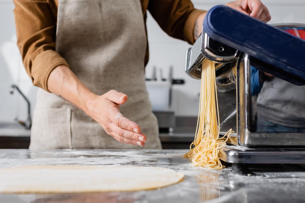 Vista ritagliata dello chef in grembiule che fa spaghetti sulla macchina della pasta - Foto, immagini