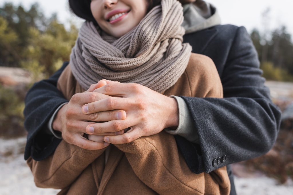 cropped view of blurred man embracing and holding hands of smiling woman during autumn walk - Photo, Image