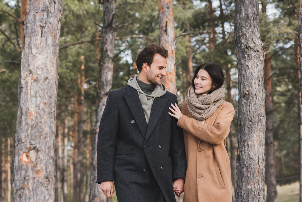 cheerful woman touching shoulder of smiling boyfriend while walking in autumn park - Photo, Image