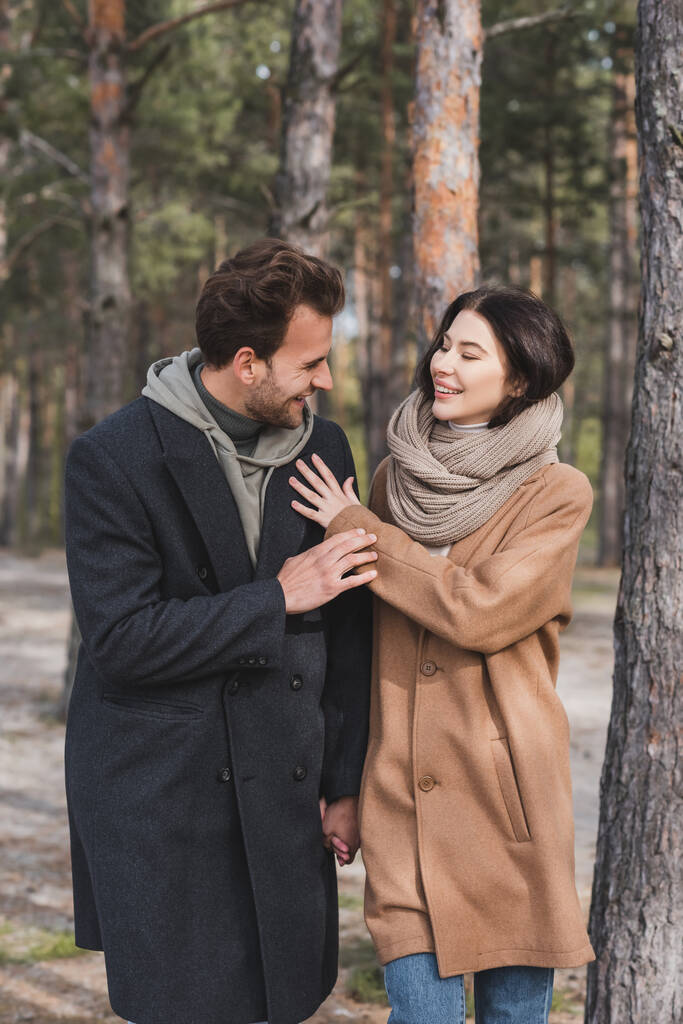 jeune couple en manteaux d'automne souriant tout en marchant dans la forêt - Photo, image
