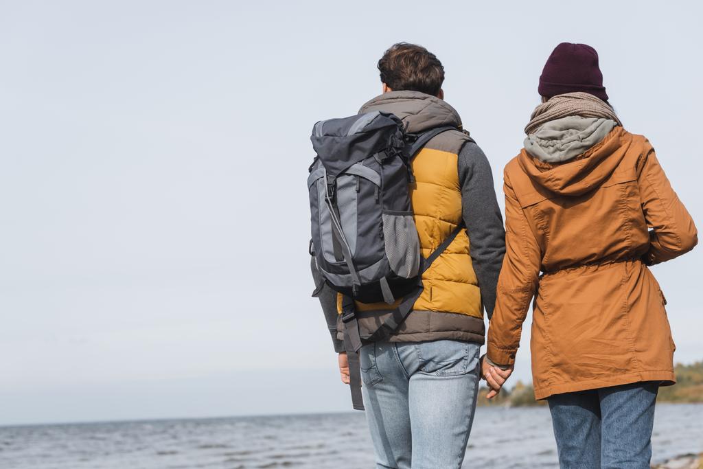 visão traseira do casal em roupa de outono de mãos dadas enquanto caminhadas perto do rio - Foto, Imagem