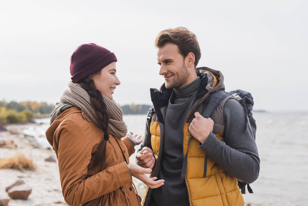 mujer joven haciendo gestos mientras habla con su novio sonriente mientras camina al aire libre - Foto, imagen