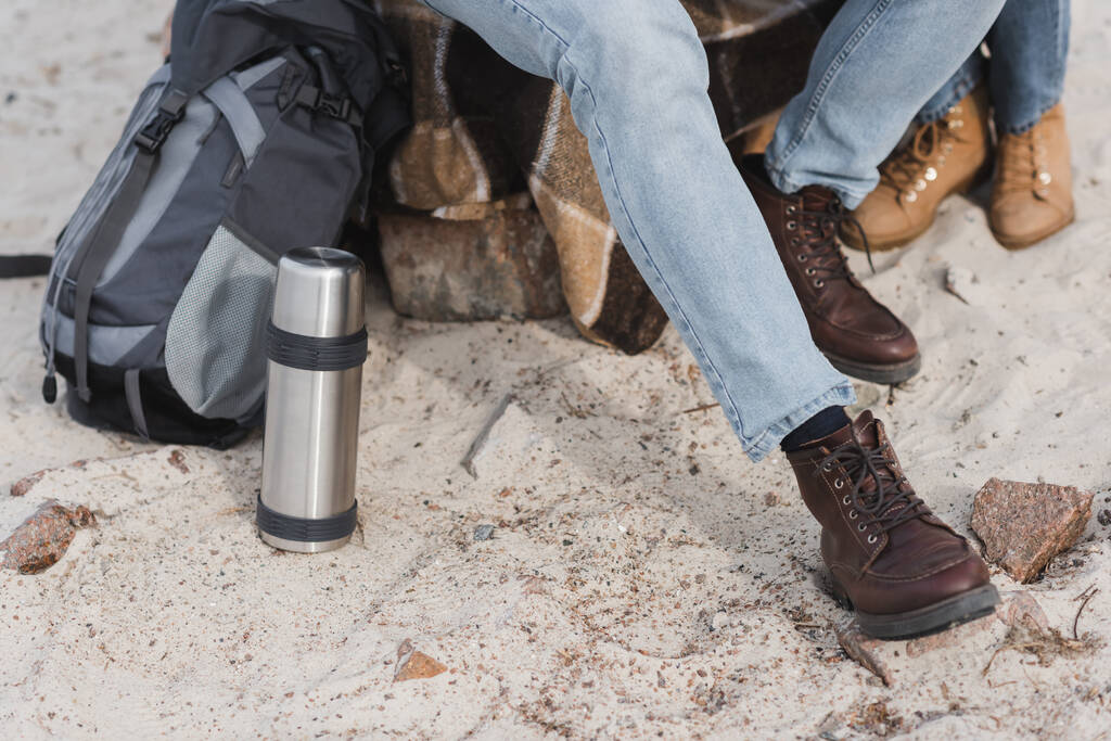 par de caminhantes sentados perto de garrafa térmica e mochila durante a parada ao ar livre - Foto, Imagem