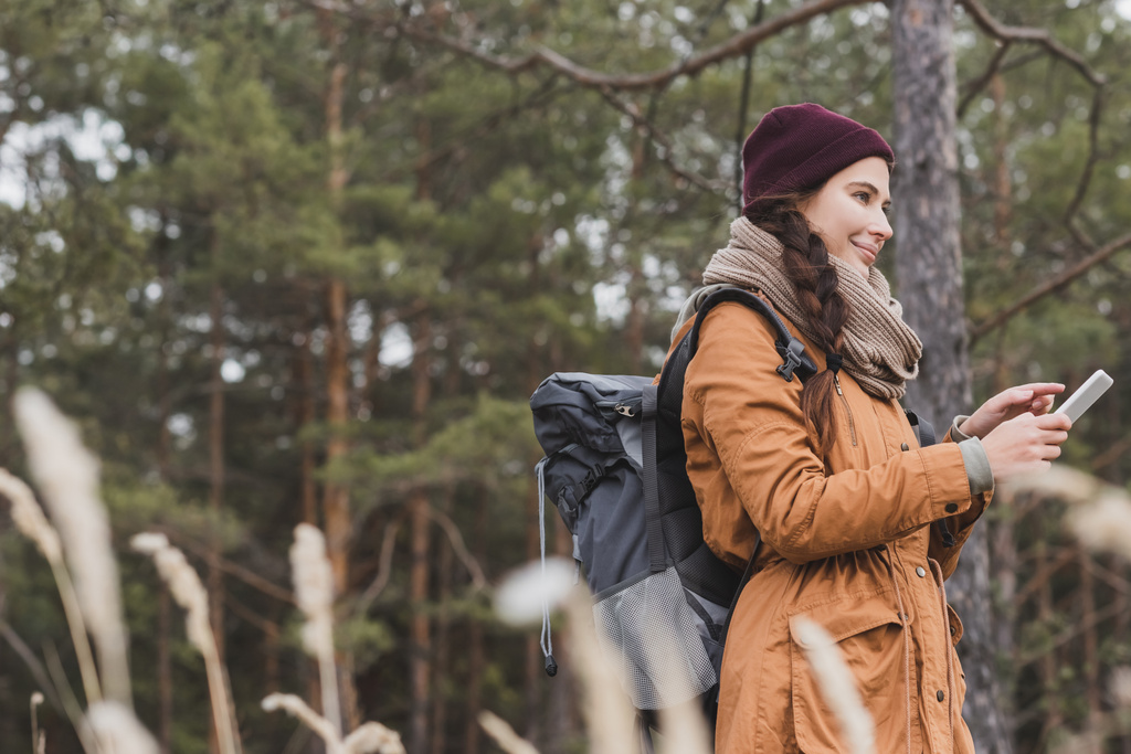 радісна жінка з рюкзаком вказує на смартфон під час пошуку напрямку в лісі
 - Фото, зображення