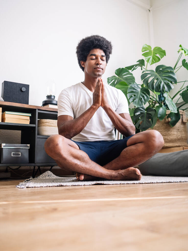 Pystysuora kuva mustasta miehestä, jolla on kiharat hiukset meditoimassa talossaan. - Valokuva, kuva