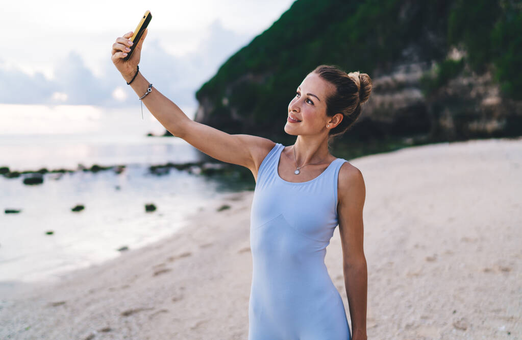 Sorgenfreies Mädchen mit Handy, das Selfie-Bilder beim morgendlichen Training am Strand klickt, Millennial Bloggerin Shooting Einfluss Video zum Teilen in sozialen Netzwerken sportive Web-Lektion - Foto, Bild