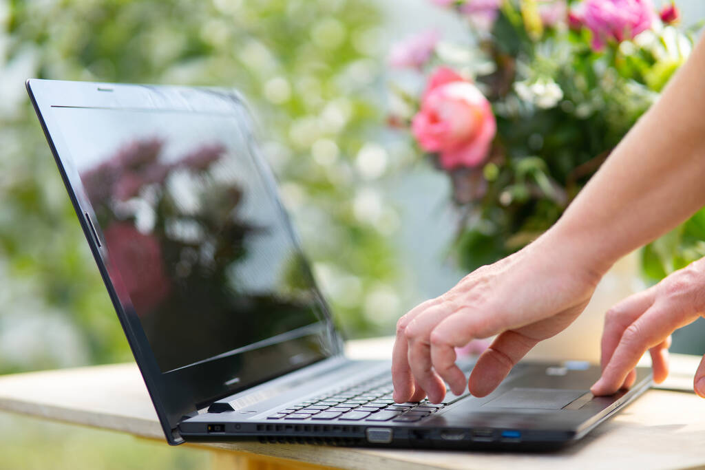 Gros plan des doigts sur un clavier d'ordinateur portable, une fleuriste femme prend des commandes en ligne pour la livraison de bouquets de fleurs. - Photo, image