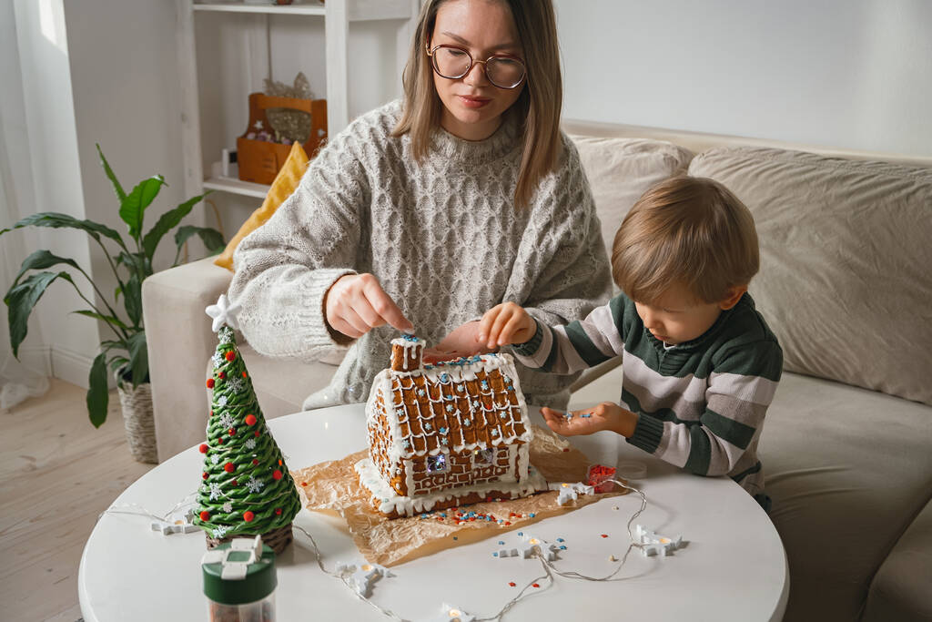 Enfant avec maman décorant ensemble la maison de pain d'épice de Noël, les activités familiales et les traditions de Noël et du Nouvel An - Photo, image