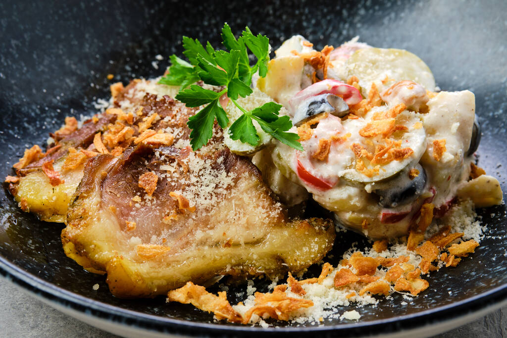 Nahaufnahme von eingelegten Gurken mit gekochten Kartoffeln und Oliven serviert mit gebratenen Schweinebauch Scheiben auf einem Teller - Foto, Bild