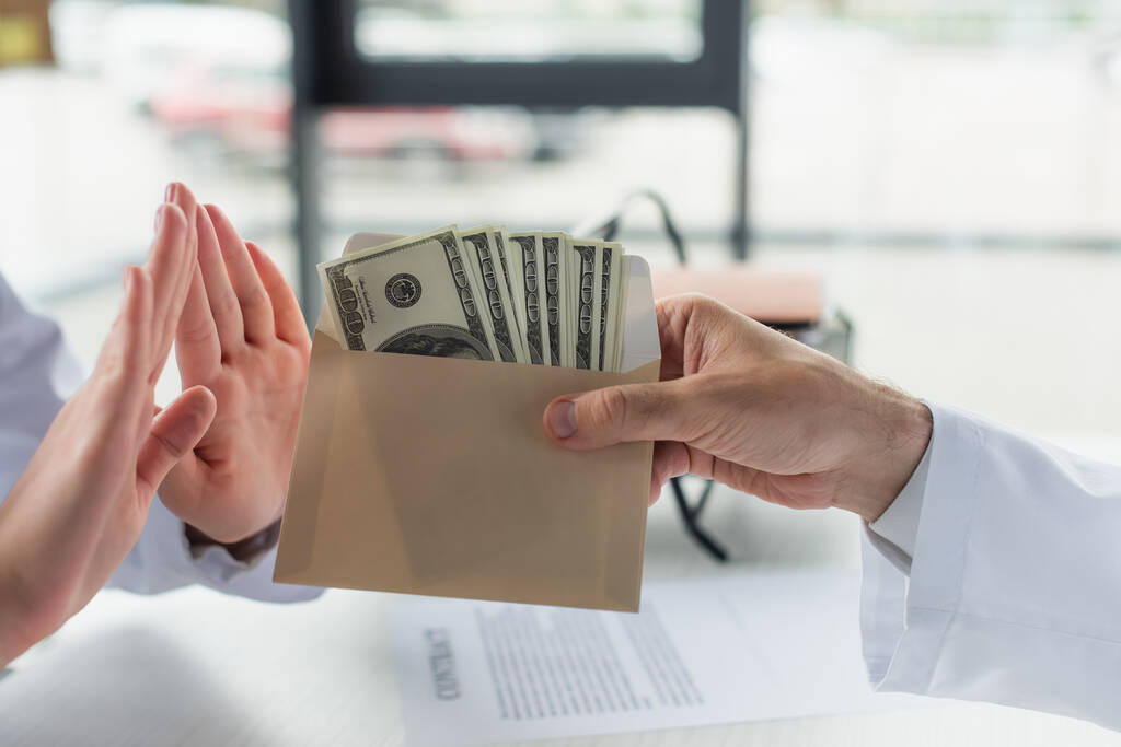 visão parcial do médico mostrando gesto de recusa perto do envelope com suborno, conceito anti-corrupção - Foto, Imagem