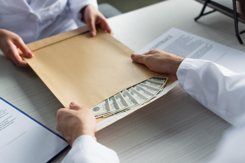 przycięty widok lekarza biorącego kopertę z pieniędzmi od pacjenta, koncepcja antykorupcyjna - Zdjęcie, obraz