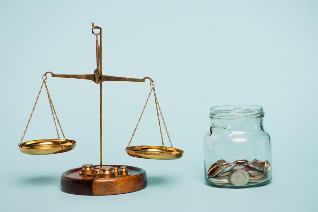 bronze justice scales near glass jar with coins on blue background, anti-corruption concept - Photo, Image