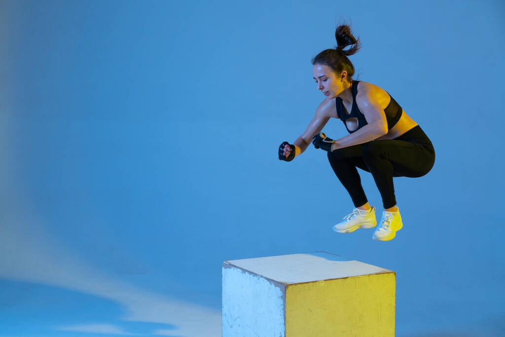 Молодая спортивная женщина прыгает на кубе. Неоновый свет в студии. - Фото, изображение