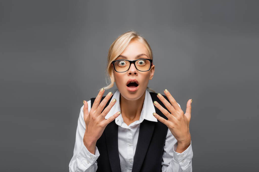 Shocked businesswoman in eyeglasses looking at camera isolated on grey  - Photo, Image