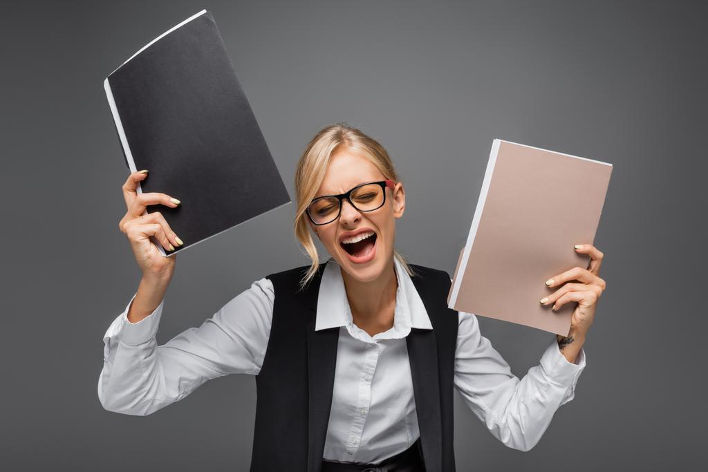 Stres podnikatelka drží papírové složky, zatímco křičí izolované na šedé  - Fotografie, Obrázek