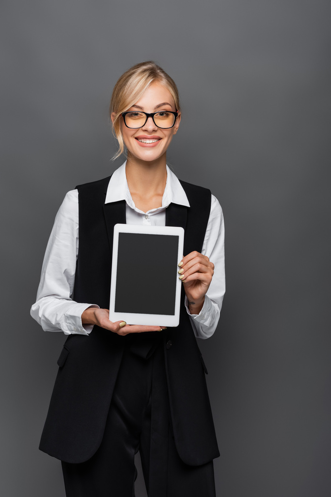 Pozytywna bizneswoman w okularach trzymająca cyfrowy tablet z pustym ekranem odizolowanym na szaro  - Zdjęcie, obraz