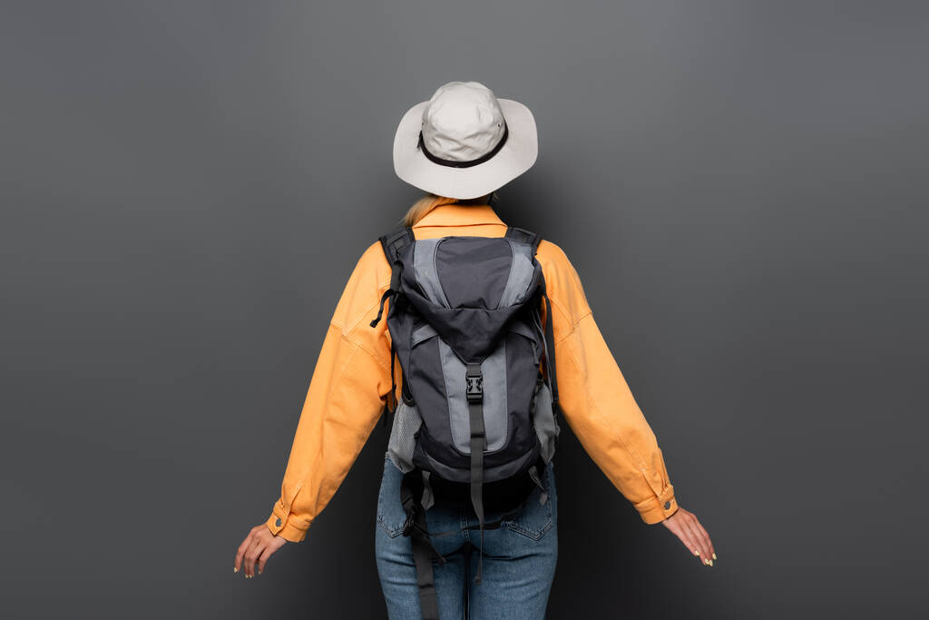 Vista trasera del turista con la mochila de pie sobre fondo gris  - Foto, imagen
