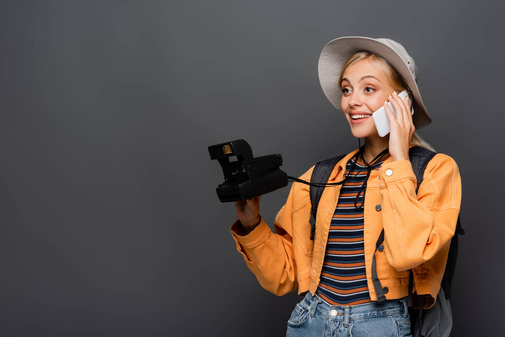 Blondi turisti hattu puhuu älypuhelimeen ja pitämällä vintage kamera eristetty harmaa  - Valokuva, kuva