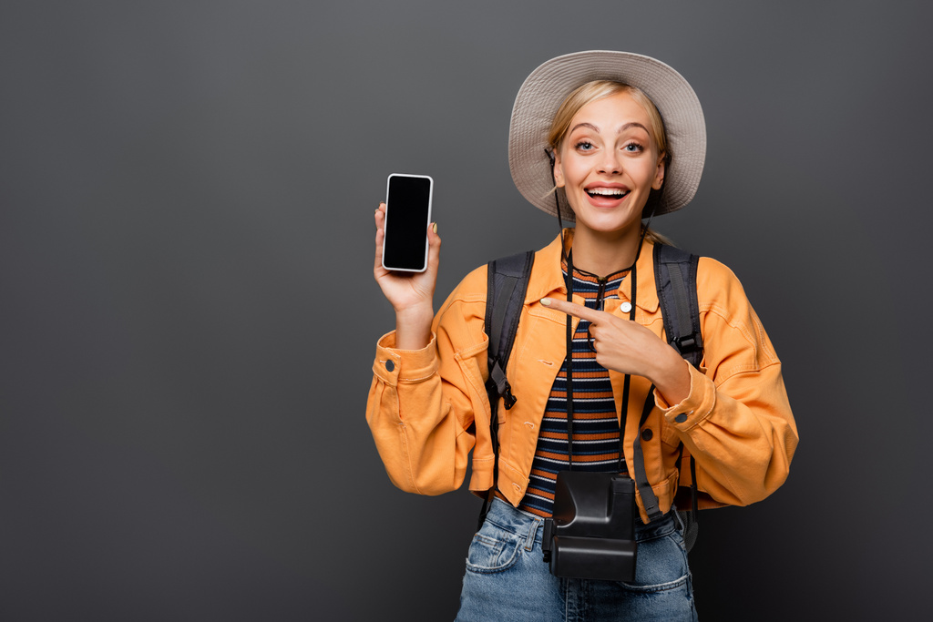 Positiver Tourist mit Oldtimer-Kamera, die auf Smartphone auf grauem Hintergrund zeigt - Foto, Bild