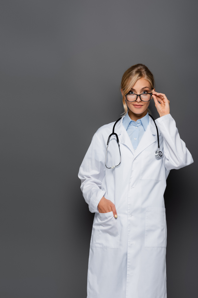 Giovane medico in possesso di occhiali e guardando la fotocamera isolata su grigio  - Foto, immagini