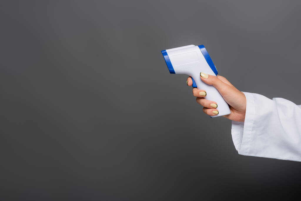 Обрізаний вид лікаря, який тримає пірометр ізольовано на сірому
  - Фото, зображення
